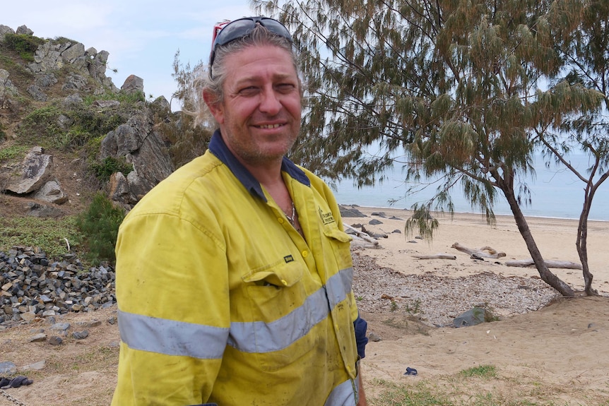 A man in a yellow and blue shirt is standing by the beach