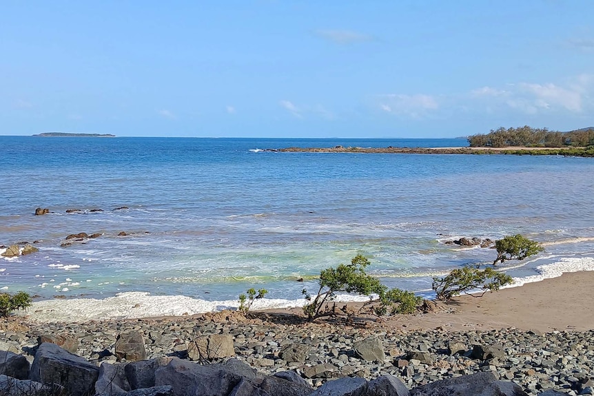 A beach scene with a rocky shoreline showing the water pink, green and blue due to algae