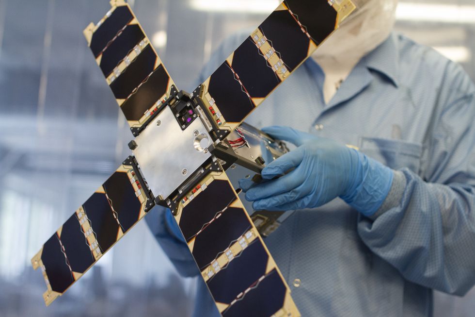 A scientist holding a miniature satellite in a laboratory